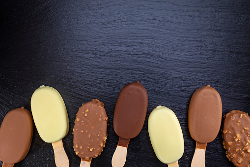 Ice cream on stick covered with chocolate on black stone slate board.