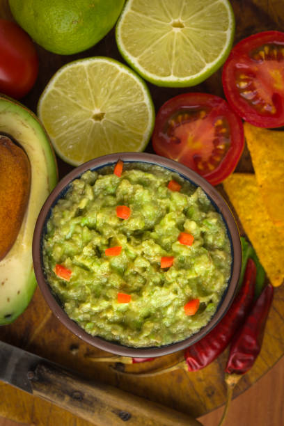 istock Guacamole in blue bowl on natural rustic desk with ingredient: lemon, tomatoes, peppers around. 991418328