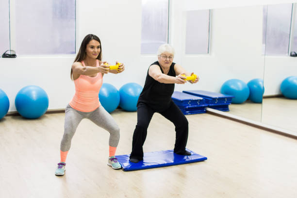 istock Female trainer helping senior woman doing exercise 991434836