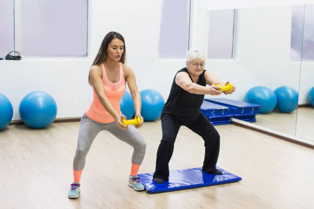 istock Female trainer helping senior woman doing exercise 991435144