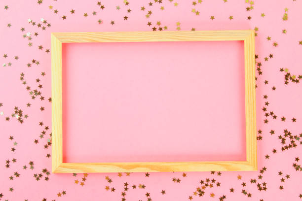 istock A wooden empty frame on a pastel background surrounded by shiny decorative stars and balls. 991440154