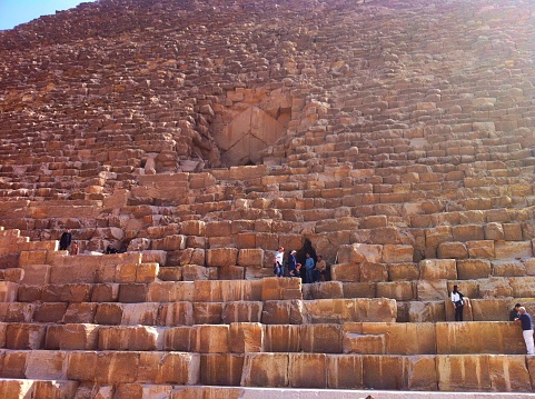 Giza, Cairo, Egypt - March 6, 2013: Visitors on stone blocks around the entrance of The Great Pyramid of Giza and an Egyptian man is checking for the tickets by sitting on a chair.