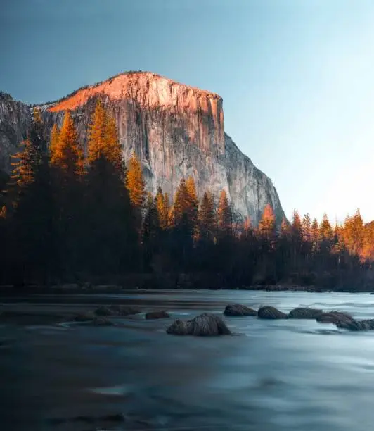 The beauty of Yosemite National Park shines during sunset by the river. The snow cover peaks and juicy tones color the landscape, flowing water weaves through this hidden place.