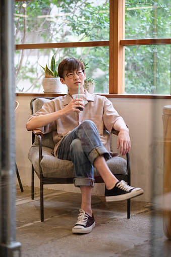 portrait of Chinese young man sitting and drinking glass of coffee