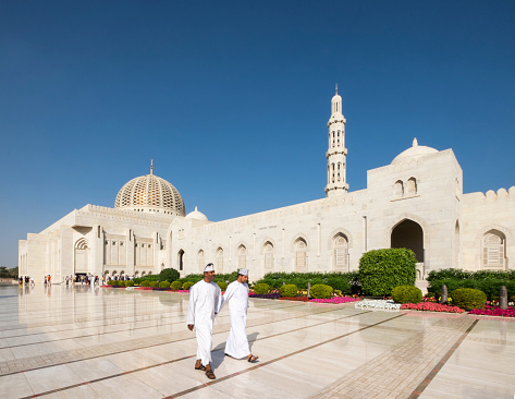 Sultan Qaboos Grand Mosque, Muscat, Oman - January 06, 2016: Two men wearing traditional Omani clothing walking past the Grand Mosque in Muscat.