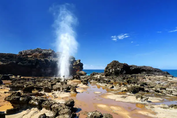Tourists admiring the Nakalele blowhole on the Maui coastline. A jet of water and air is violently forced out through the hole in the rocks. Hawaii, USA.
