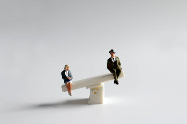 A miniature man and woman sitting on a mini seesaw. stock photo