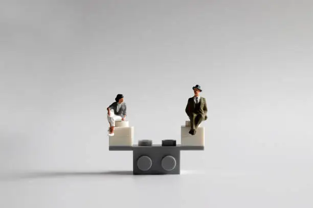 The concept of equality of opportunity for men and women. A miniature man and woman sitting on a mini seesaw.