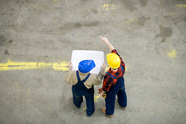 istock High angle view of unrecognizable engineers in hardhats and overalls analyzing construction plan and discussing building project at site 991676410