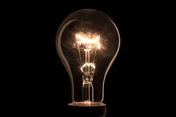 Realistic light bulb on the black background. Lamp light in the dark. Electric bulb. Glowing light in the dark.