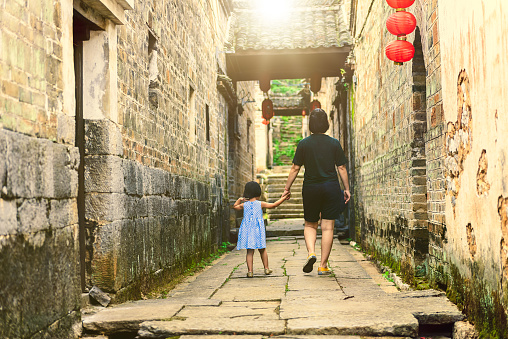A Chinese girl walking forward and mother look at her back in Chinese ancient town.Guilin,China.