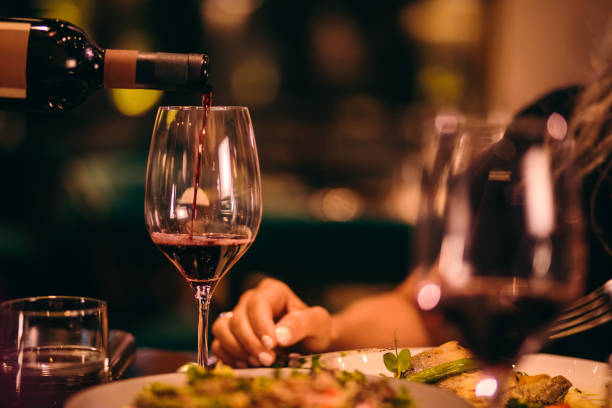 nahaufnahme des sommeliers servieren rotwein im fine-dining restaurant - essen am tisch stock-fotos und bilder