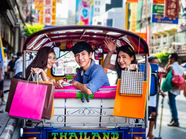 travel concept.group of happy friend are traveling.tourist holding shopping bag sitting in tuk tuk thai traditional taxi with blurring china town bangkok background.