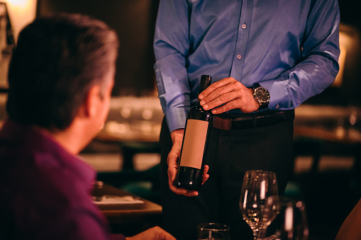 Waiter showing wine bottle to man before serving in glasses at luxurious gourmet restaurant