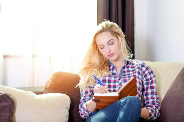 istock Young woman writing in her notebook on at home 991816380