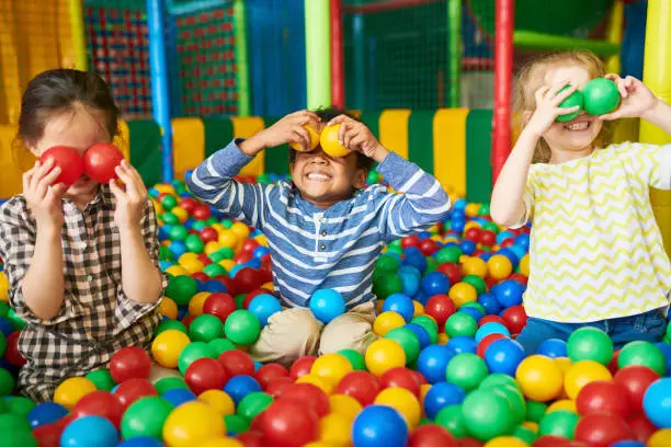 Portrait of three funny little kids playing in ball pit and enjoying time in childrens entertainment and play area, copy space