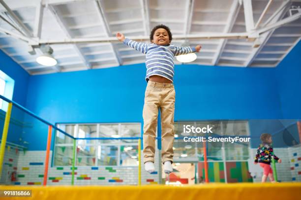 Chico Afroamericano Disfrutar De Camas Elásticas Foto de stock y más banco de imágenes de Trampolín - Artículos deportivos - Trampolín - Artículos deportivos, Niño, Interior