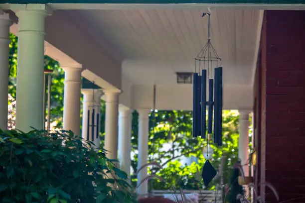 Wind chimes hanging from a house with white pillars in the deck area on a sunny day