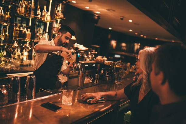 бармен делает коктейли в ретро-баре для зрелой пары - retro revival couple men elegance стоковые фото и изображения