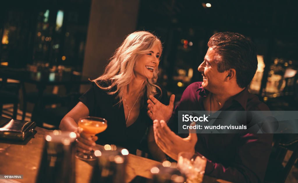 Senior husband and wife laughing and having drinks at bar embracing Couple - Relationship Stock Photo