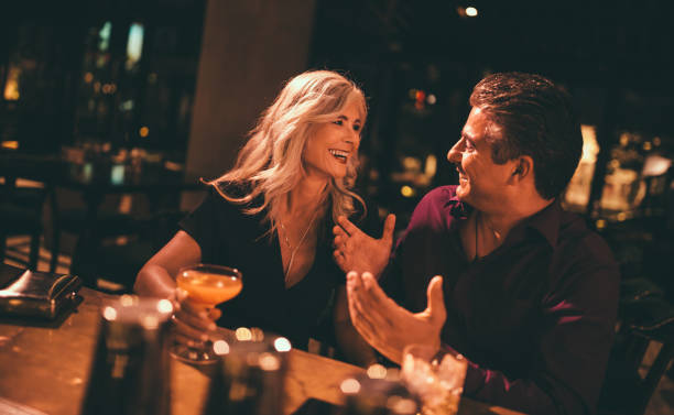 Senior husband and wife laughing and having drinks at bar embracing bar counter photos stock pictures, royalty-free photos & images