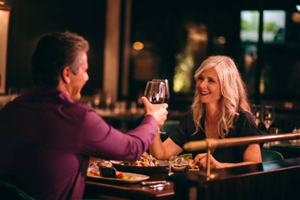 Smiling mature husband and wife toasting with wine at dinner Senior couple in love toasting with red wine and having dinner at fine dining restaurant silver service stock pictures, royalty-free photos & images