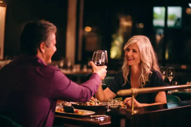 Photo of Smiling mature husband and wife toasting with wine at dinner