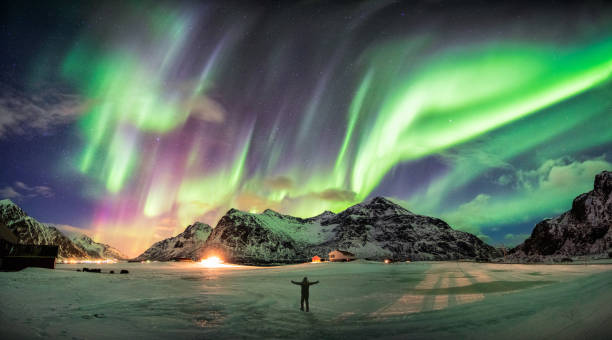 Aurora borealis (Northern lights) over mountain with one person Aurora borealis (Northern lights) over mountain with one person at Skagsanden beach, Lofoten islands, Norway aurora polaris stock pictures, royalty-free photos & images