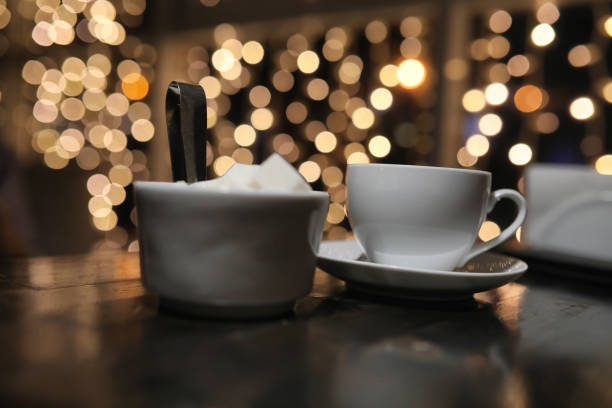 A cropped image of a woman picking up a sugar cube from a white jar in a restaurant, highlighting the concept of poor nutrition and lifestyle.