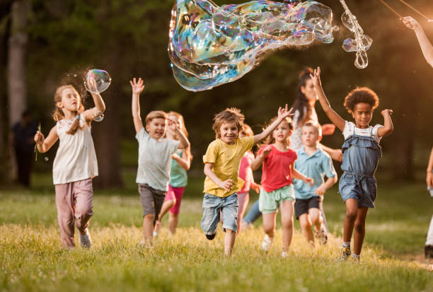 lúdico a los niños divertirse mientras se está ejecutando por debajo de las burbujas arco iris en la naturaleza. - bubble wand bubble child playful fotografías e imágenes de stock