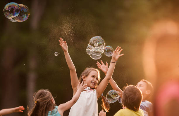 Carefree kids having fun while catching bubbles in nature.