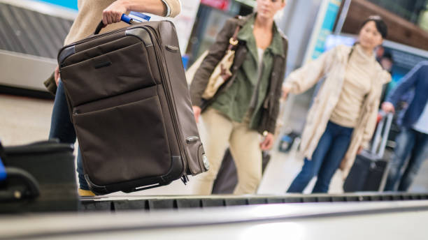 istock Female traveller picking up suitcase from baggage claim line 991877520