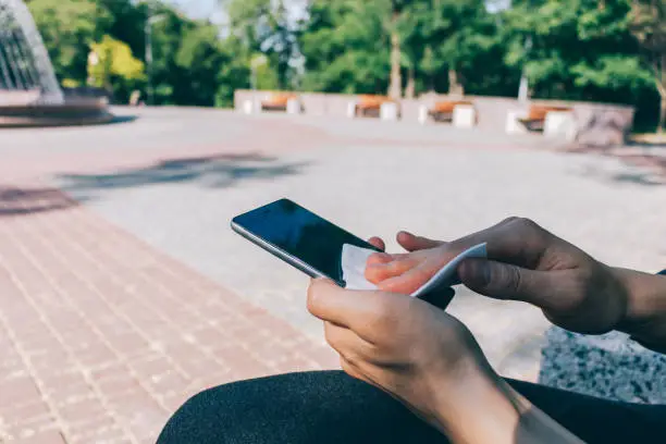 Photo of Woman cleaning display of smart phone with antibacterial tissue