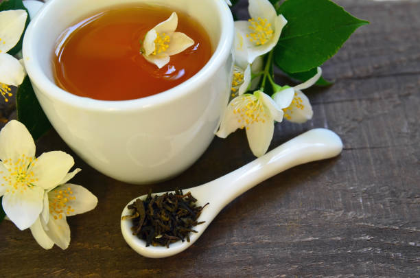 jazmín té verde seco deja en una cuchara con flores de jazmín y taza de té en el fondo de madera vieja. bebida sana, dieta o concepto de fitoterapia. - jasmine tea jasmine herbal tea drink fotografías e imágenes de stock