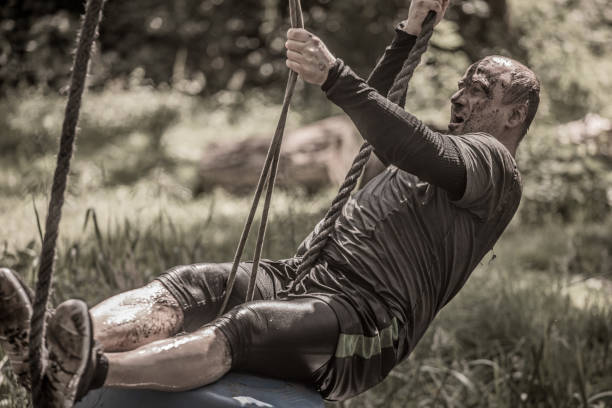 istock Individual man having sporty fun on a rope climb at a public mud run obstacle course 991971338