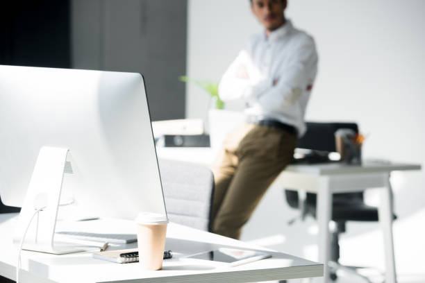 istock close-up view of desktop computer and paper cup, man leaning at table behind 991972358