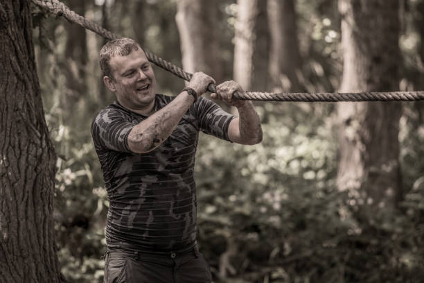 istock Individual man having sporty fun on a rope climb at a public mud run obstacle course 991977662
