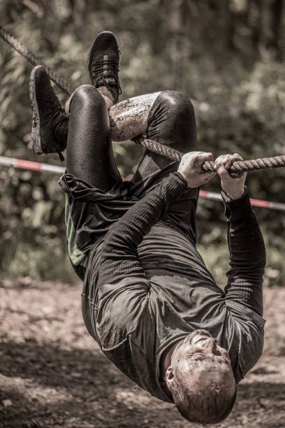 istock Individual man having sporty fun on a rope climb at a public mud run obstacle course 991977788