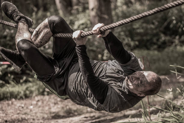 istock Individual man having sporty fun on a rope climb at a public mud run obstacle course 991978052