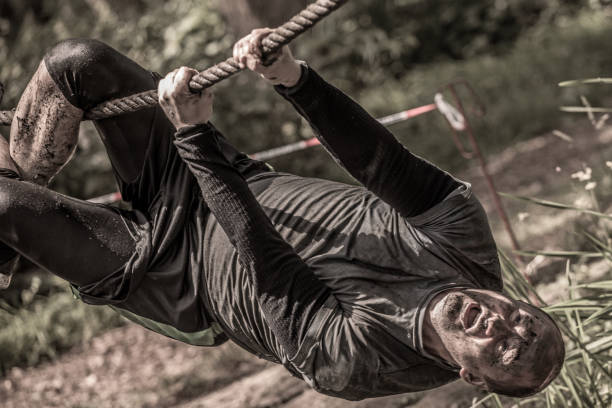 istock Individual man having sporty fun on a rope climb at a public mud run obstacle course 991978634