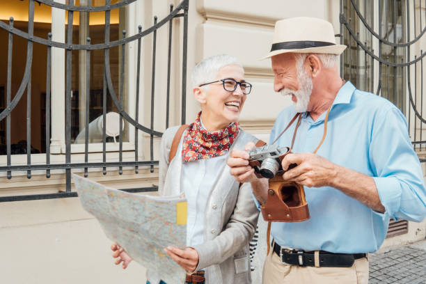 istock Older woman with the map looking at the man with camera 991997740