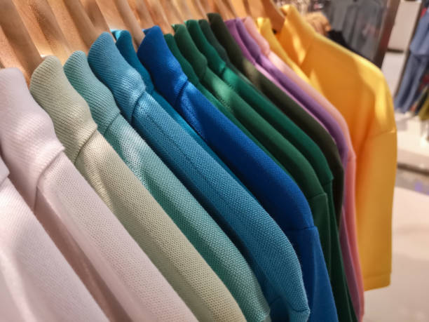 мужские разноцветные рубашки поло, в самых разных оттенках цветов, свисающих со стойки в универмаге. - polo shirt multi colored clothing variation стоковые фото и изображения