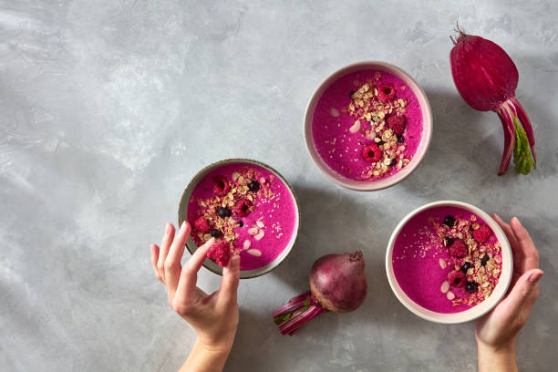 istock Fresh vegetable smoothies from beets, berries and oatmeal on a gray concrete background with copy space. Hand the girl put raspberries in a bowl. Top view 992002540