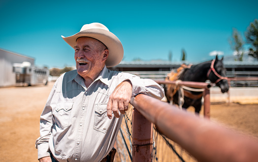 Cowboy is  leaning on a fence in rodeo arena in Utah, USA. He is holding lasso and getting ready for riding.