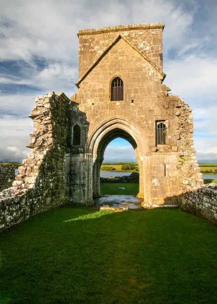 Ruins of Oratory of Saint Molaise abbey on Devenish Island with green lawn in foreground. Enniskillen, Northern Ireland