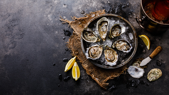 Open shucked fresh Oysters with lemon and Rose Wine in ice bucket on dark background copy space