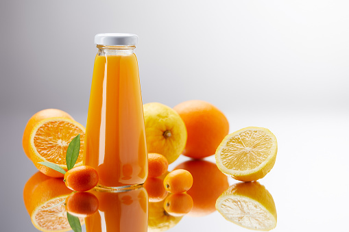 bottle of fresh juice with oranges, lemons and kumquats on reflective surface