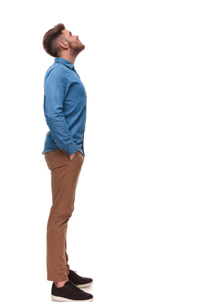 side view of relaxed casual man looking up at something while standing  on white background, full length picture