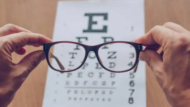 Hands holding sight glasses in front of optician sight chart.