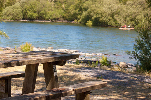 A picnic bench in dappled light, a lake in the background with a kayak in the distance